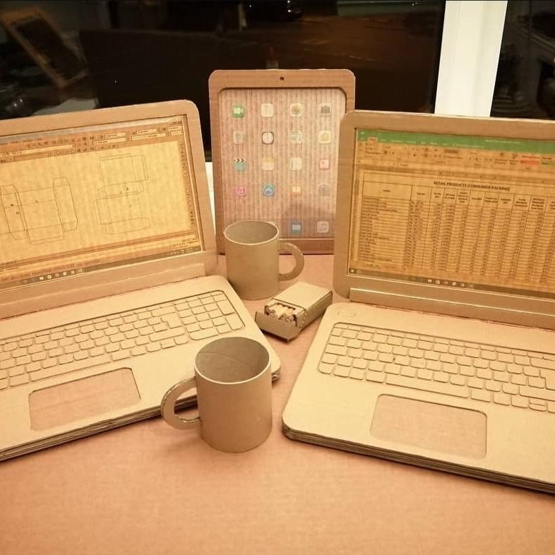 Three cardboard laptops, a tablet, and a coffee mug arranged on a table.