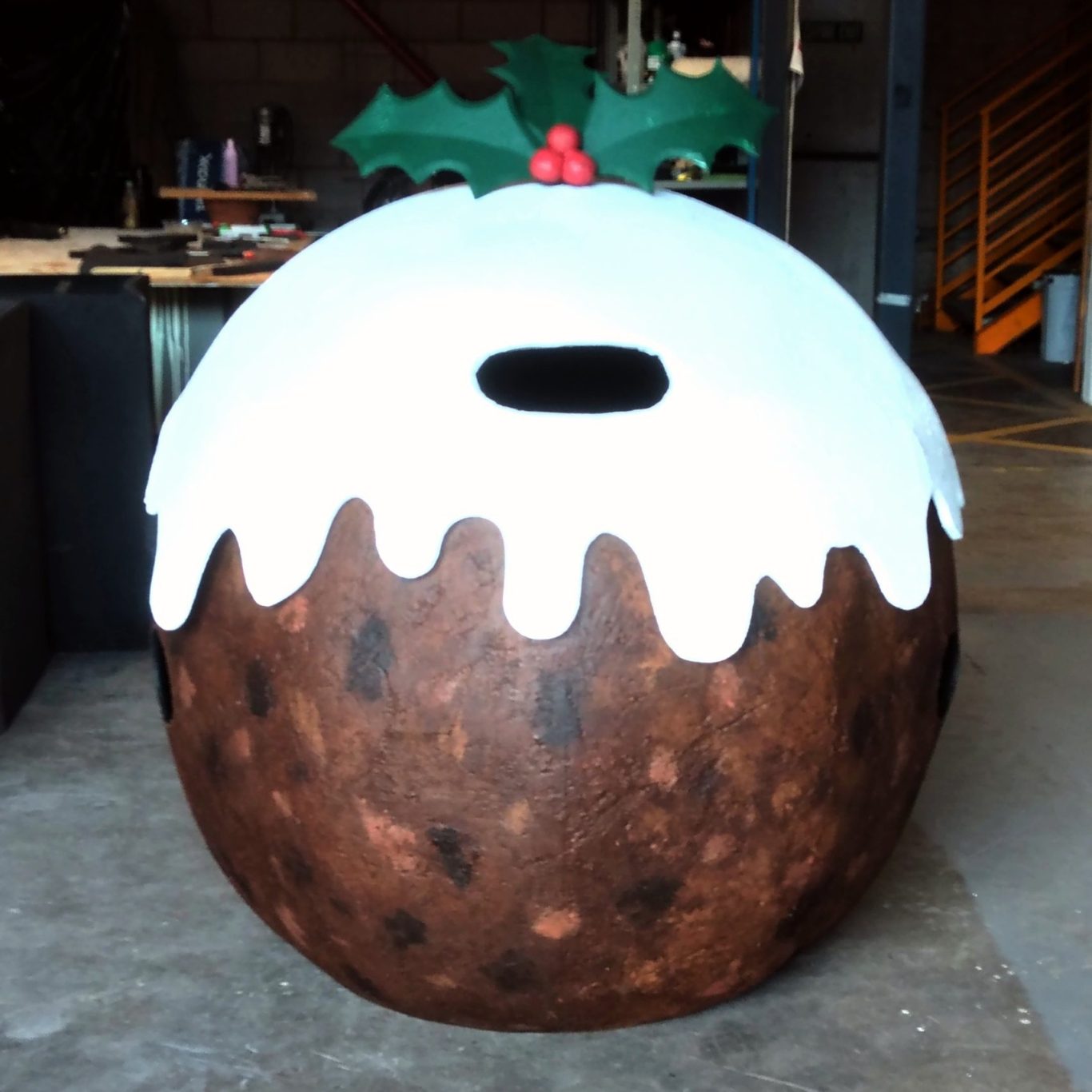 Large decorative Christmas pudding with white icing and holly on top.