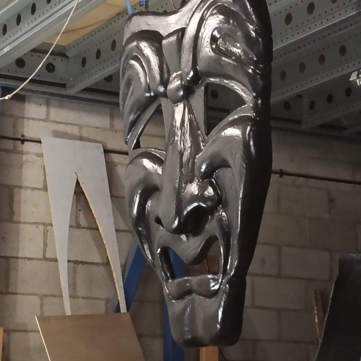 Black sculptural mask hanging in an industrial setting, showcasing intricate features.