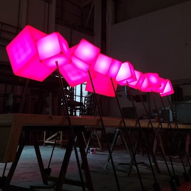 Row of glowing pink cube lights on black stands in a darkened space.